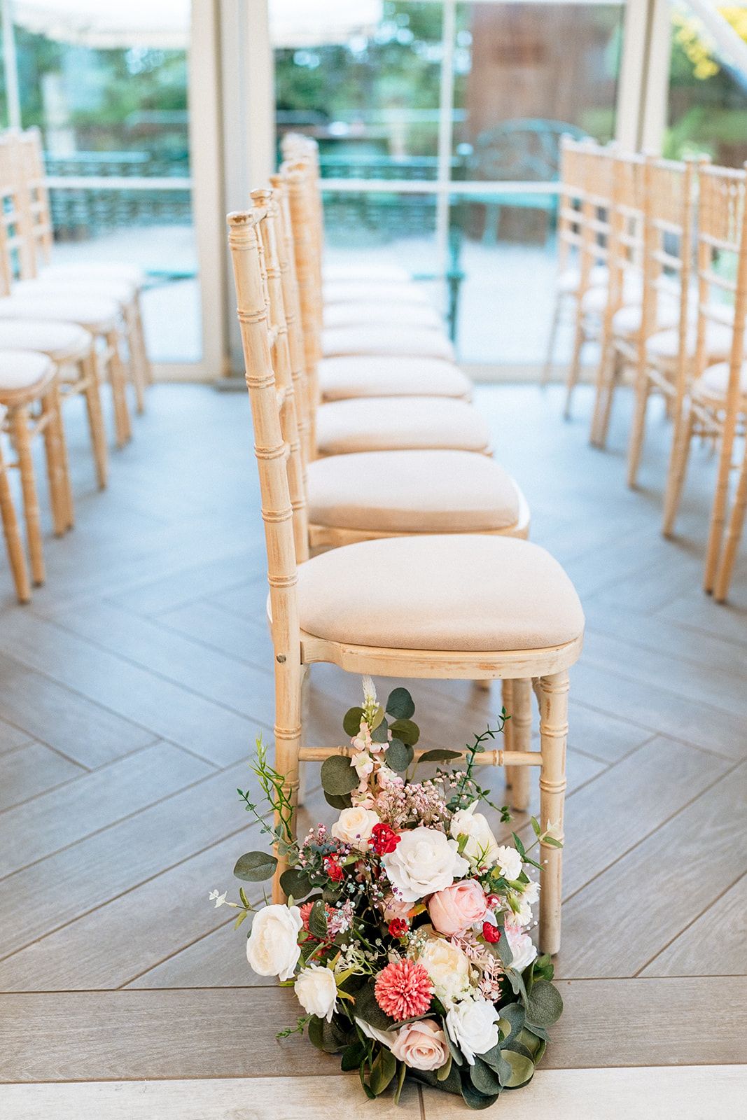 Wedding ceremony chairs with bamboo details and romantic floral arrangements in white, pink and burgundy on the floor.