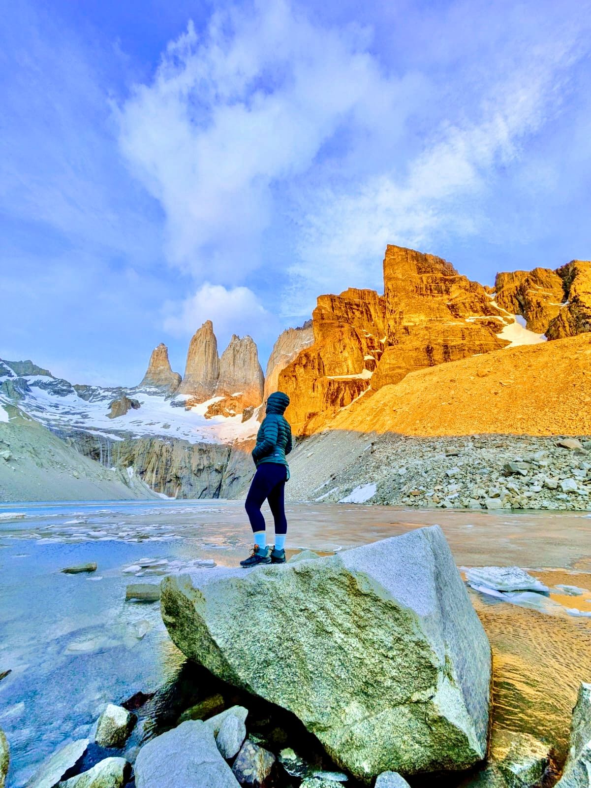 A hiker stands on rocky terrain overlooking Torres del Paine mountain peaks and glacial lake in Patagonia, Chile - Sarah Kate Photography