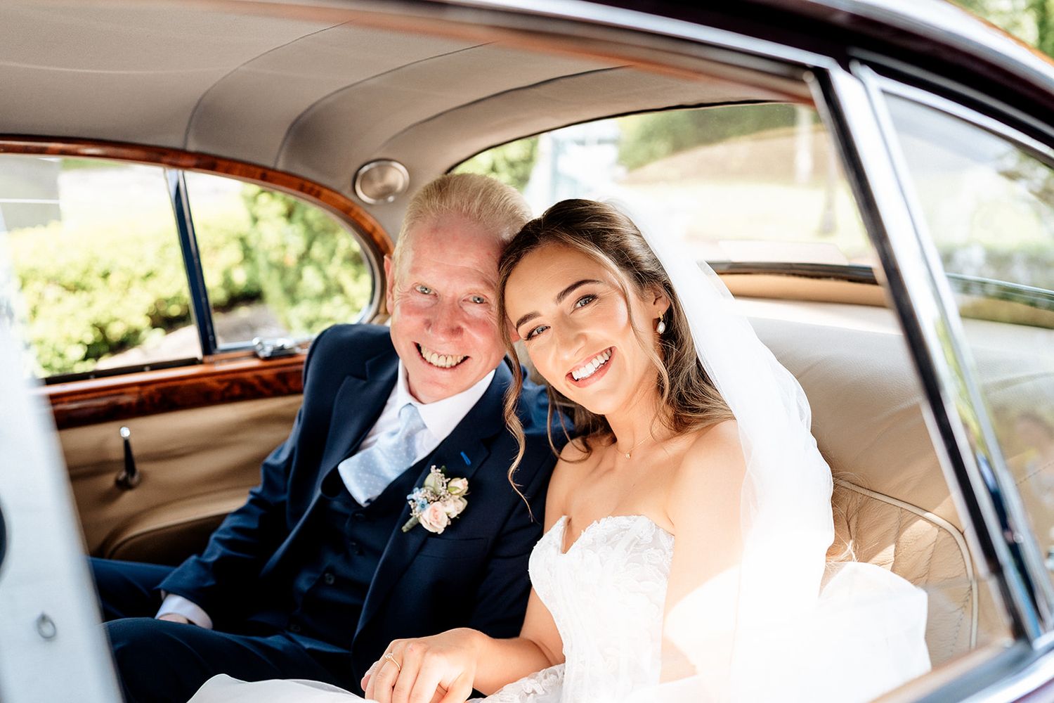 A happy couple sits together in the back seat of a vintage car on their special day.