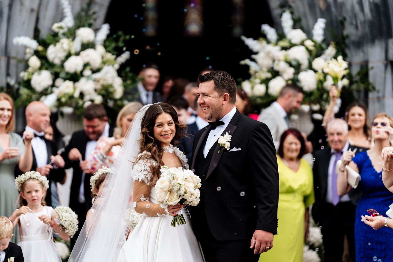 A wedding celebration scene with guests tossing confetti and flower petals outdoors amid festive cheering.