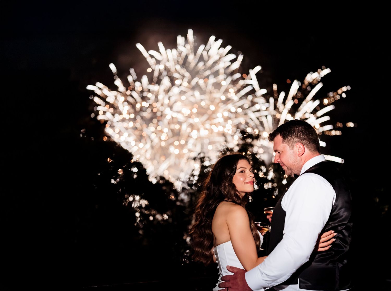 A series of elegant firework displays illuminate the night sky as silhouettes of a couple embrace during their wedding ceremony.
