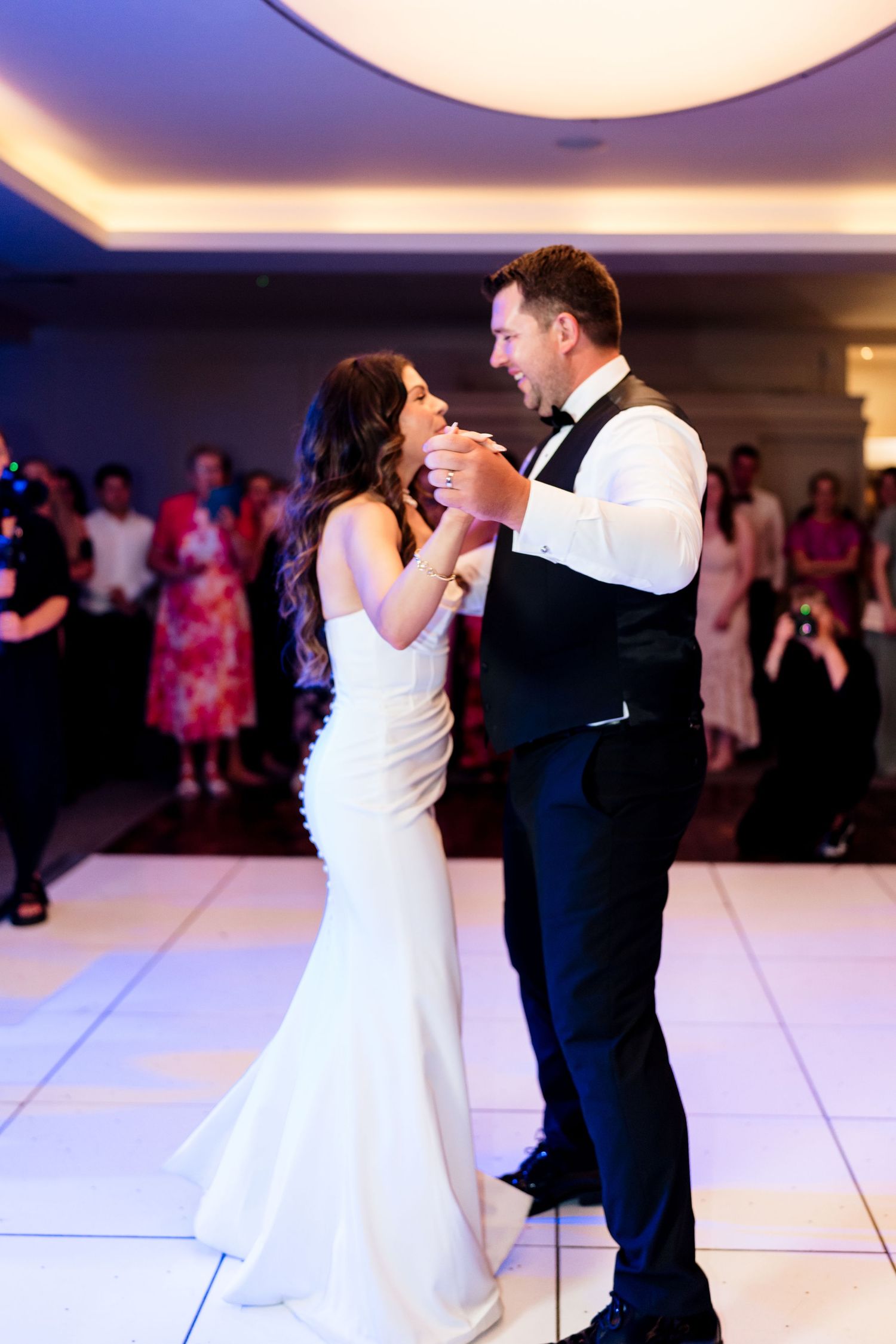 A couple shares a romantic dance together on a white dance floor during a wedding reception with purple lighting.