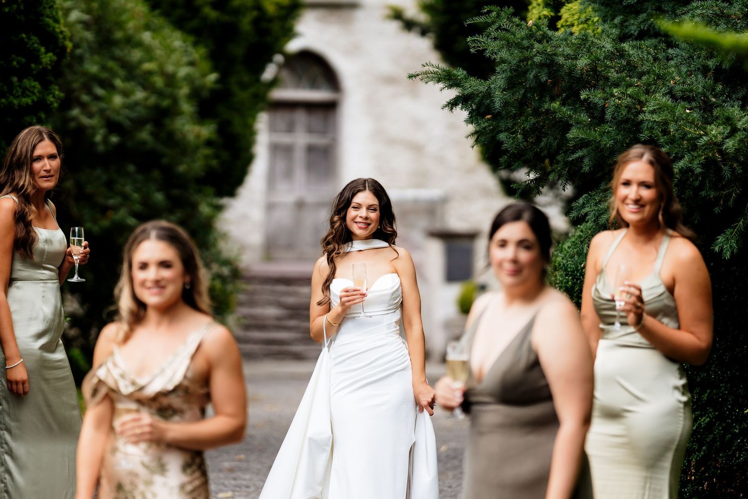 A collection of people in light colored dresses holding champagne glasses during an outdoor celebration.