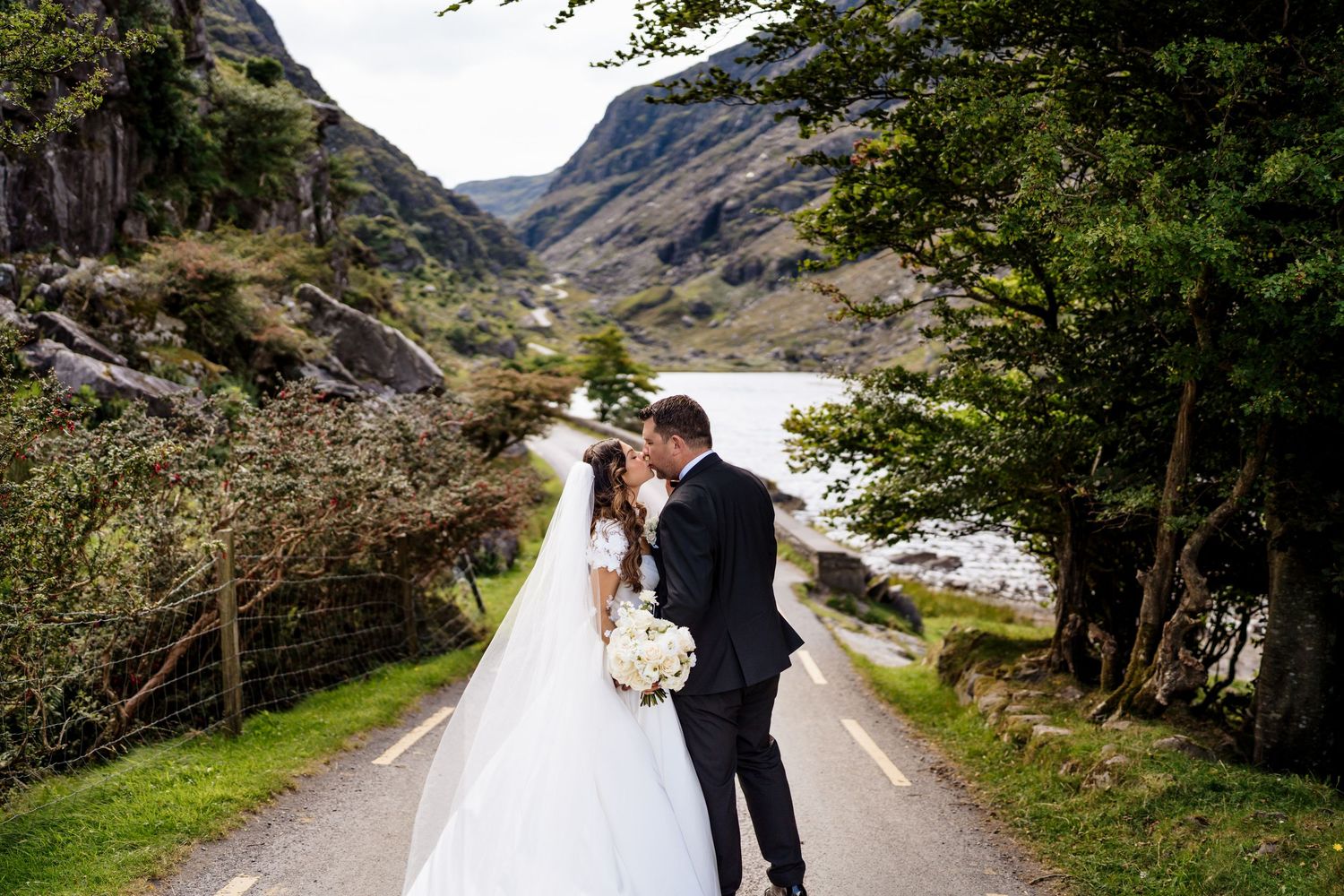 A scenic mountain road through a remote valley lined with trees and rugged cliffs creates a dramatic wedding backdrop.