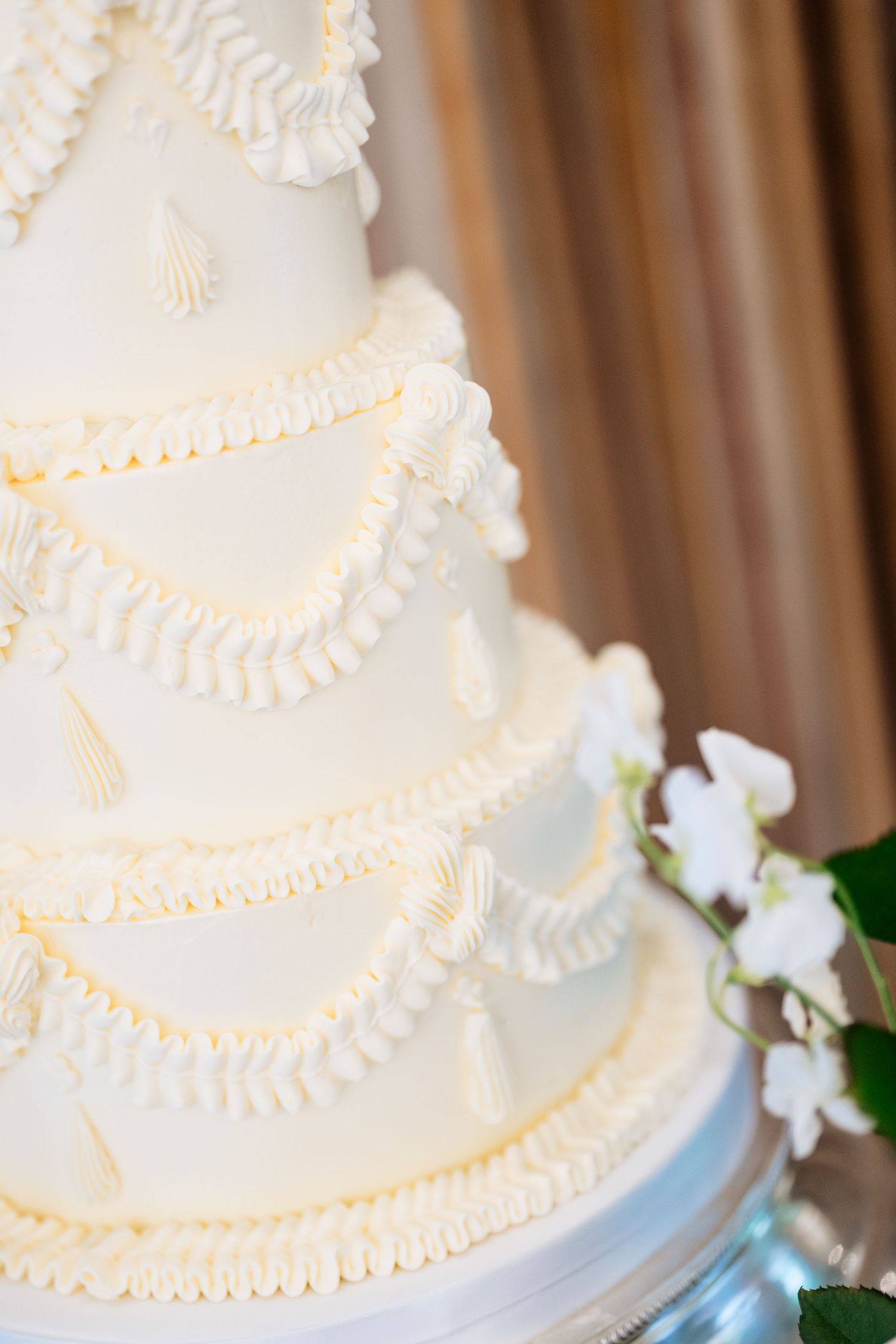 Elegant white wedding cake with delicate piped details and small white flower decorations.