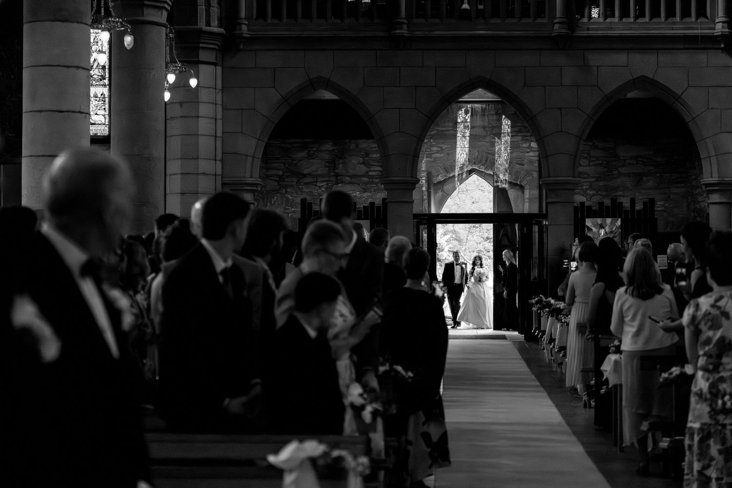 Silhouettes of people walking through an illuminated archway in a dark architectural corridor.