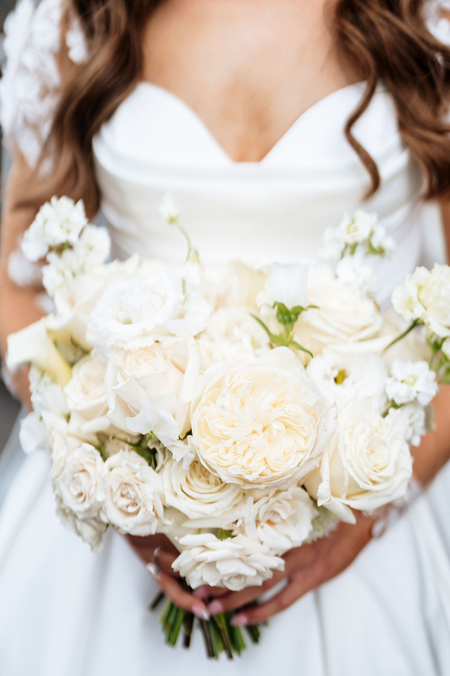 Close-up shots of elegant white and cream rose bridal bouquet held against white wedding dress fabric.