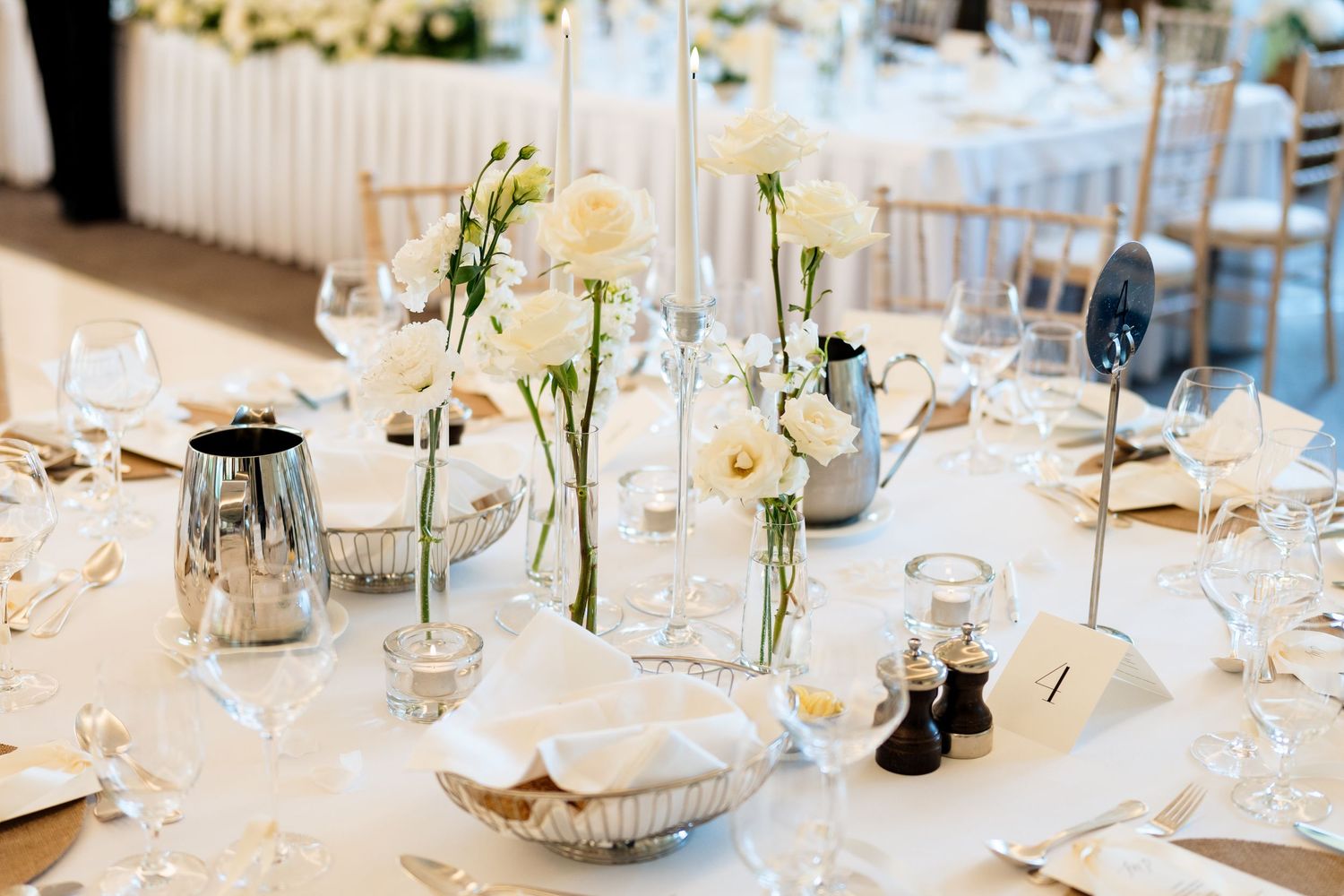 A collection of elegant wedding reception tables decorated with white floral centerpieces and glass candle holders.