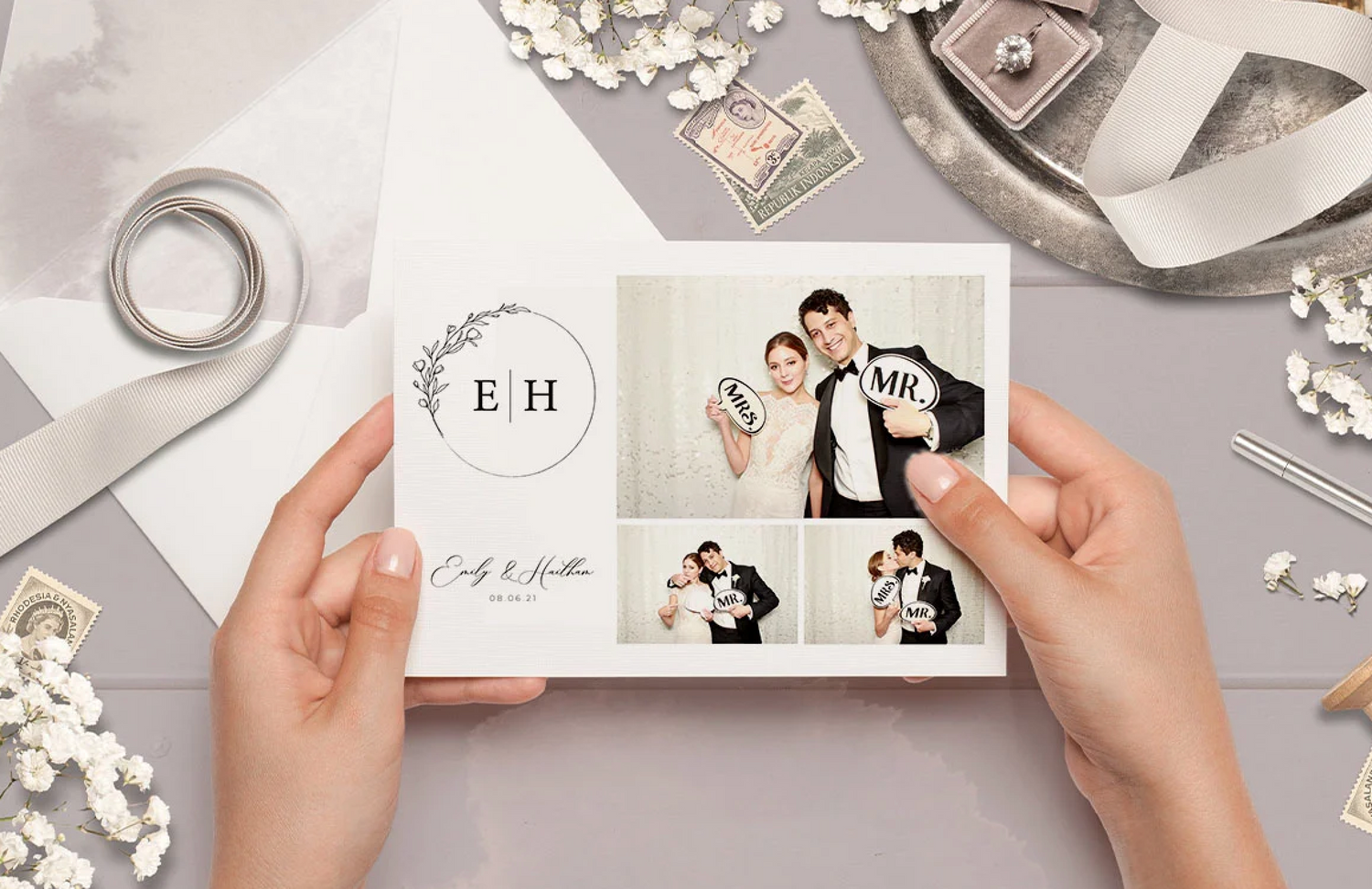 Hands flip through pages of a wedding photo album with delicate floral decorations on a light gray surface.