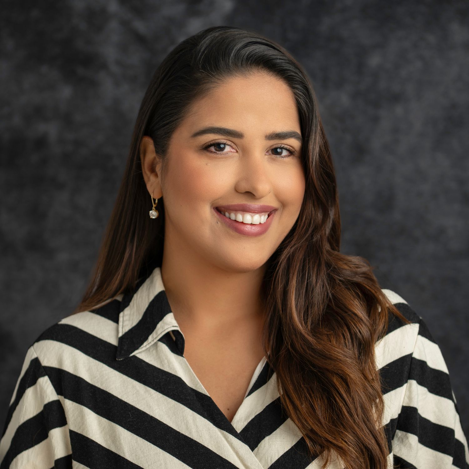 Professional portrait of woman in striped black and white blouse against dark background.