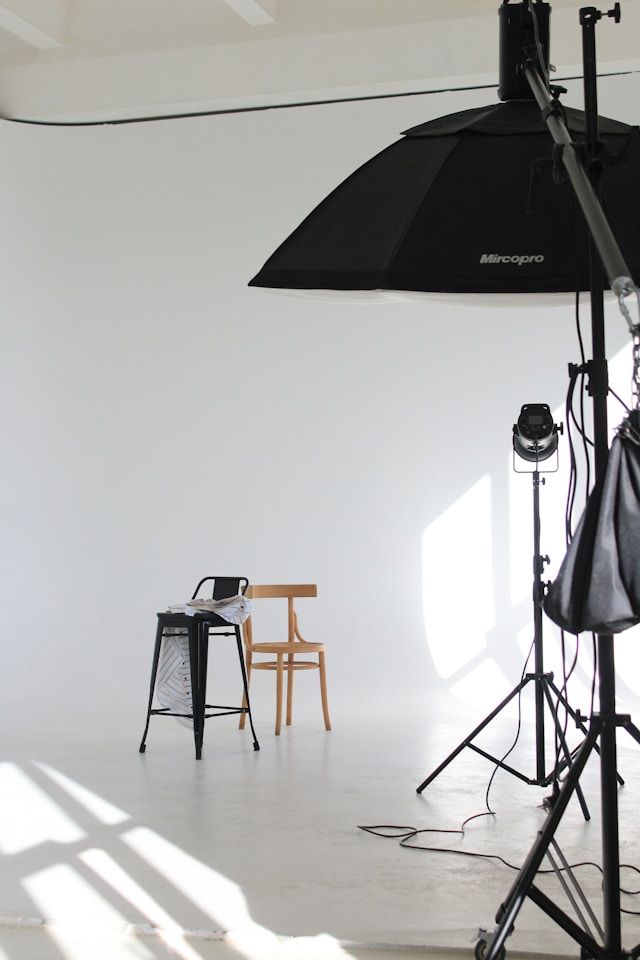 Photography studio setup with black umbrella lights and chairs against white backdrop.