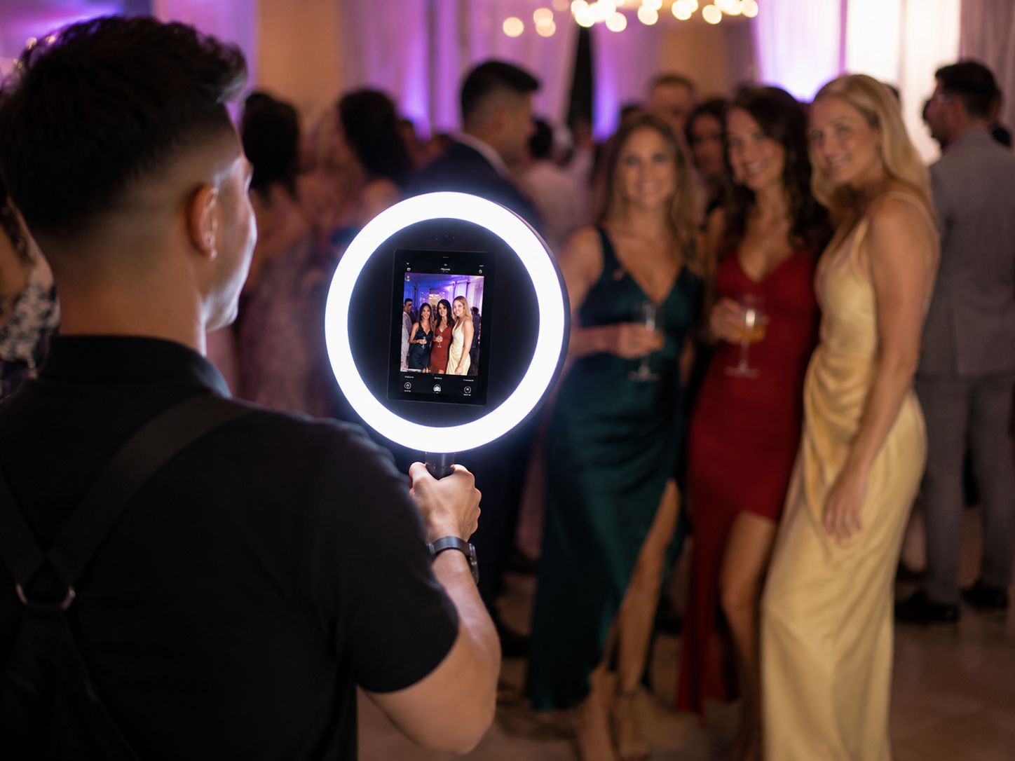 Photographer using ring light to capture three women posing at formal event in elegant dresses.