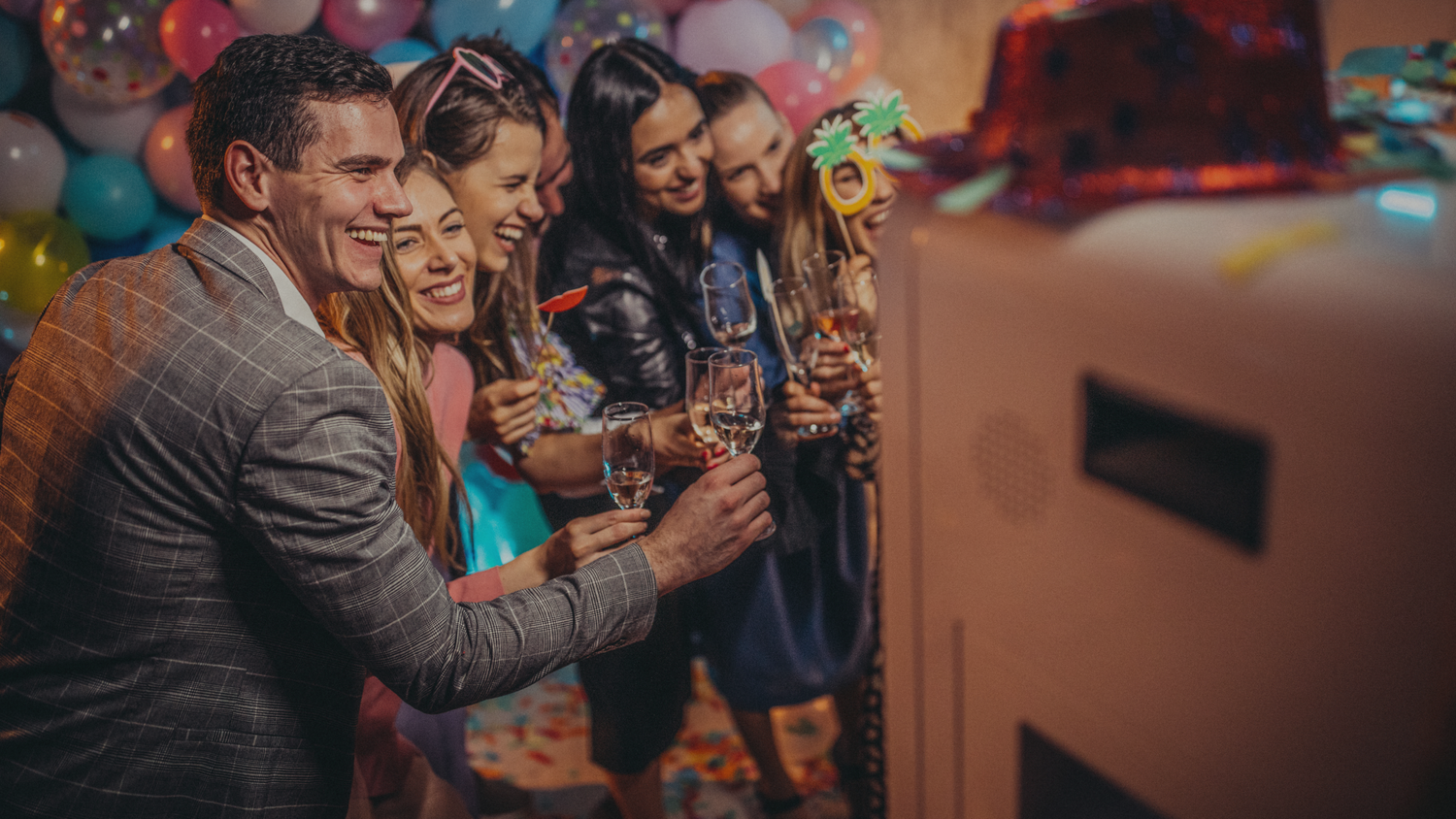 Party guests enjoying photo booth moments in warm ambient lighting.