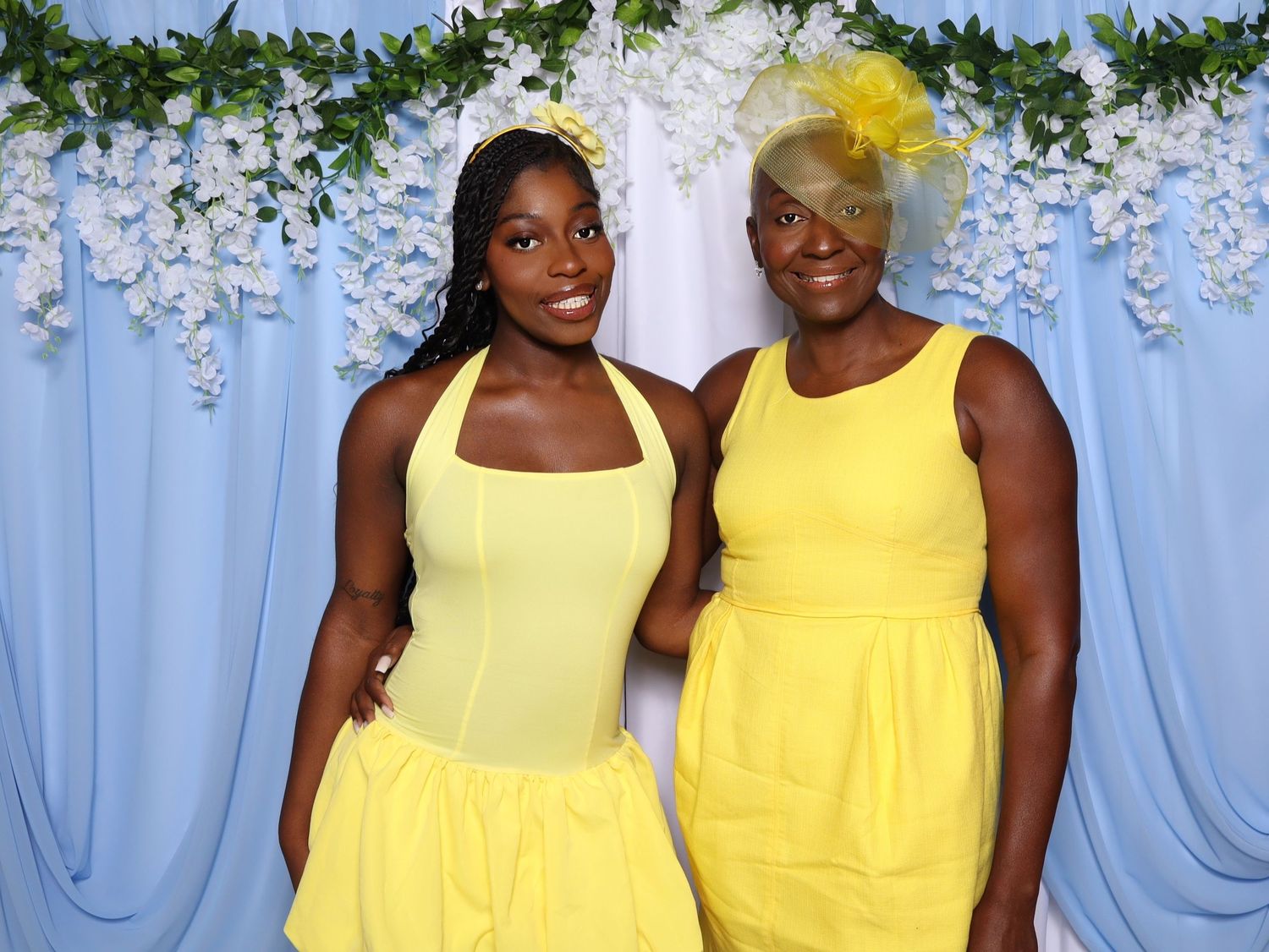 Bridesmaids in bright yellow dresses pose against a blue backdrop with floral decorations.