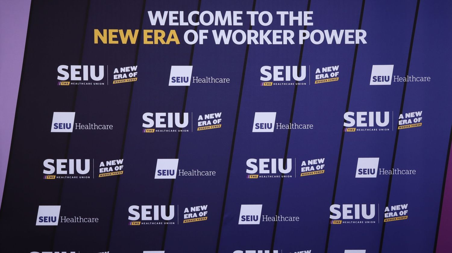 A dark blue stage backdrop with repeating SEIU union logos and text reading 'Welcome to the New Era of Worker Power'.