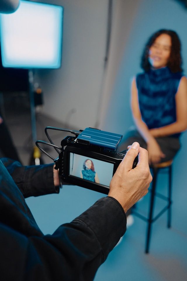 Photographer holds camera displaying woman in blue outfit on screen during professional studio photo shoot.