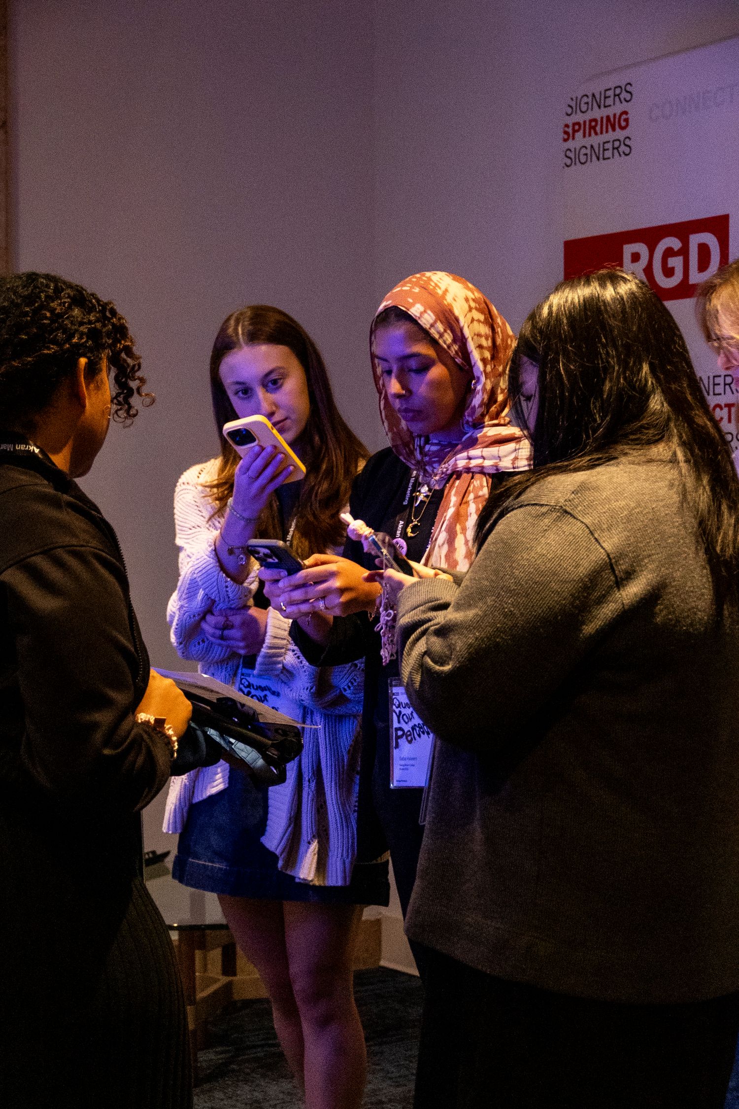 People gathered at an event space illuminated by blue lighting check their phones and socialize.