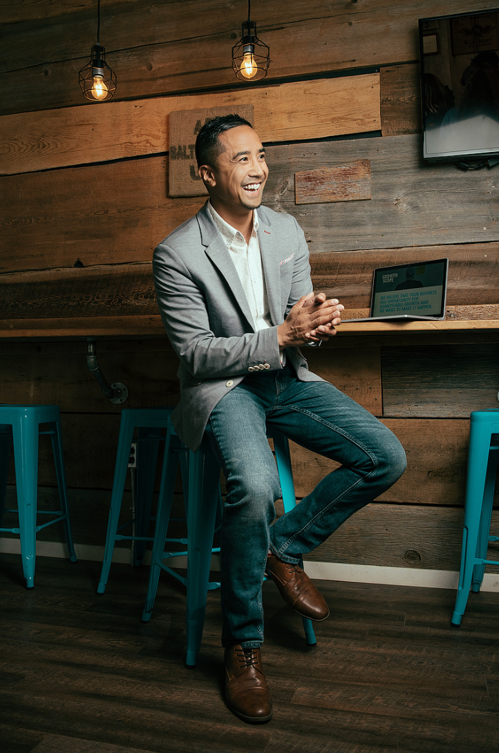 Casual business portraits in grey suit seated at wooden bar with turquoise stools.