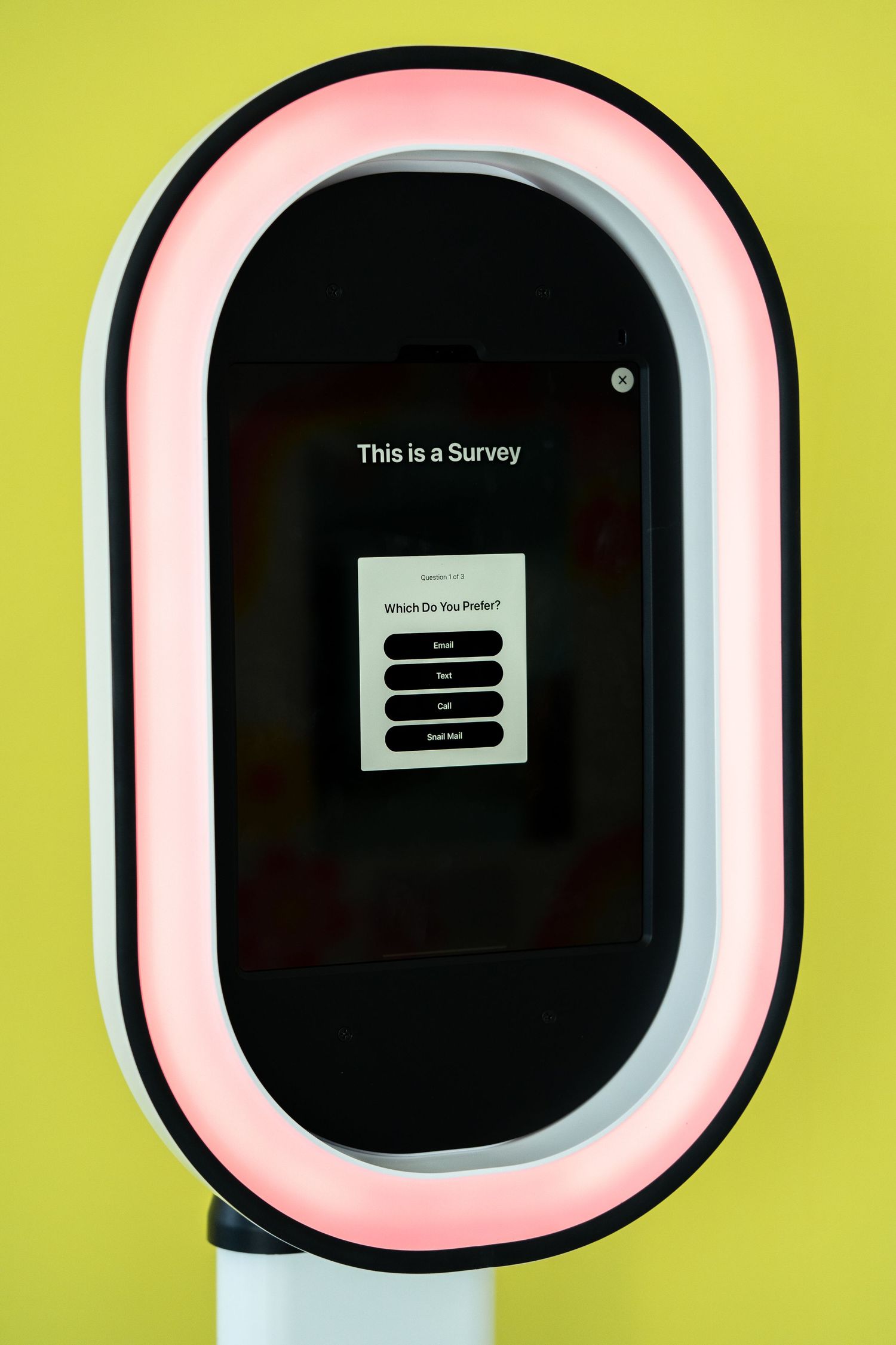 Digital survey interface shown on photo booth screen with neon pink lighting against yellow background.