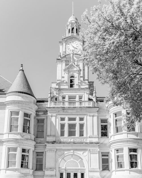 Black and white image of the historic Dallas County Iowa Courthouse with a tall clock tower, flanked by trees.