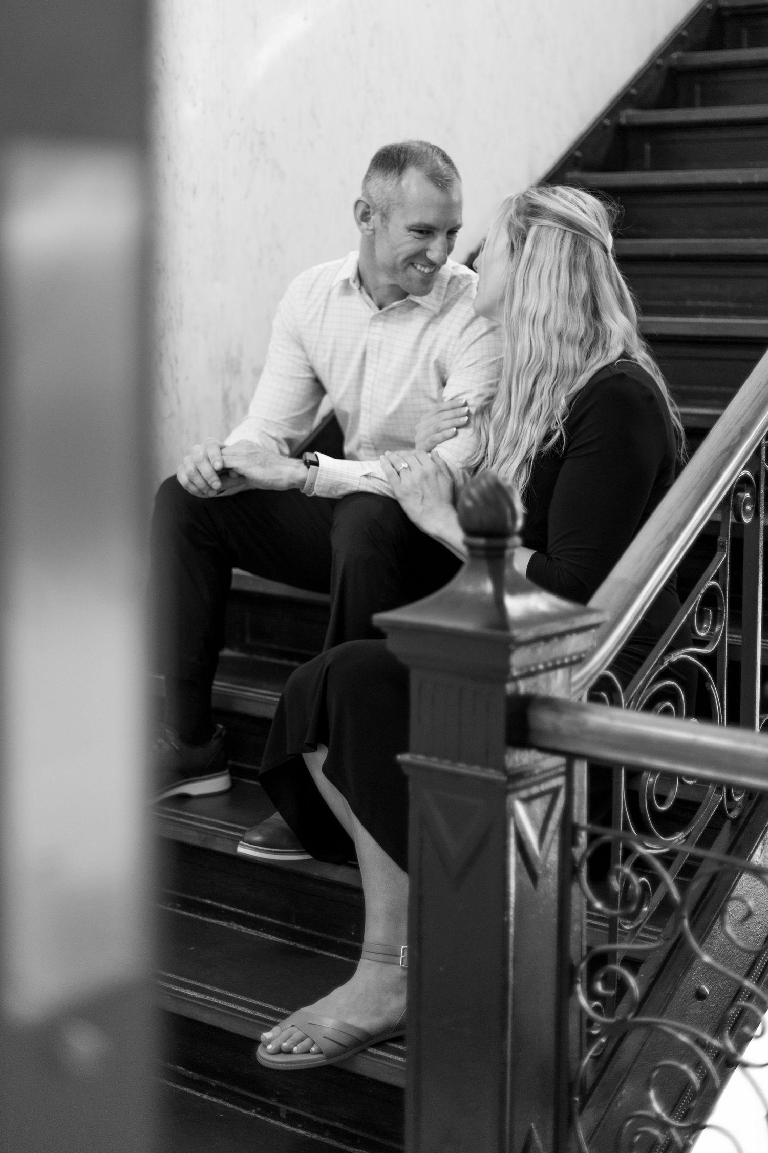 A couple sits on a staircase, smiling and holding hands after their courthouse elopement in Dallas County, Iowa.