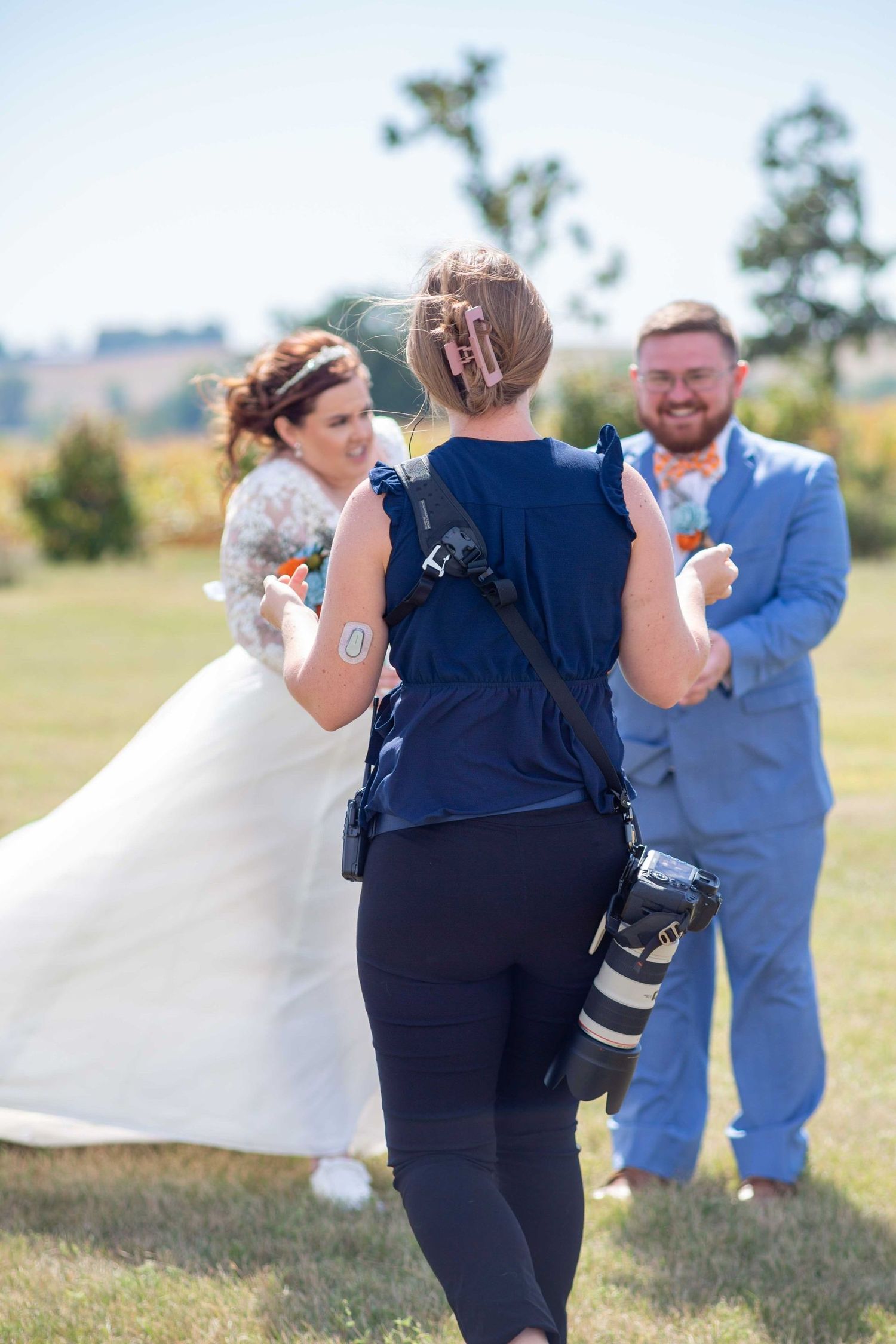 A bride in a white gown and a groom in a blue suit are directed by a photographer.