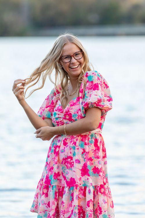 A smiling high school senior with long blonde hair stands in the water at Gray's Lake Park in Des Moines, Iowa.