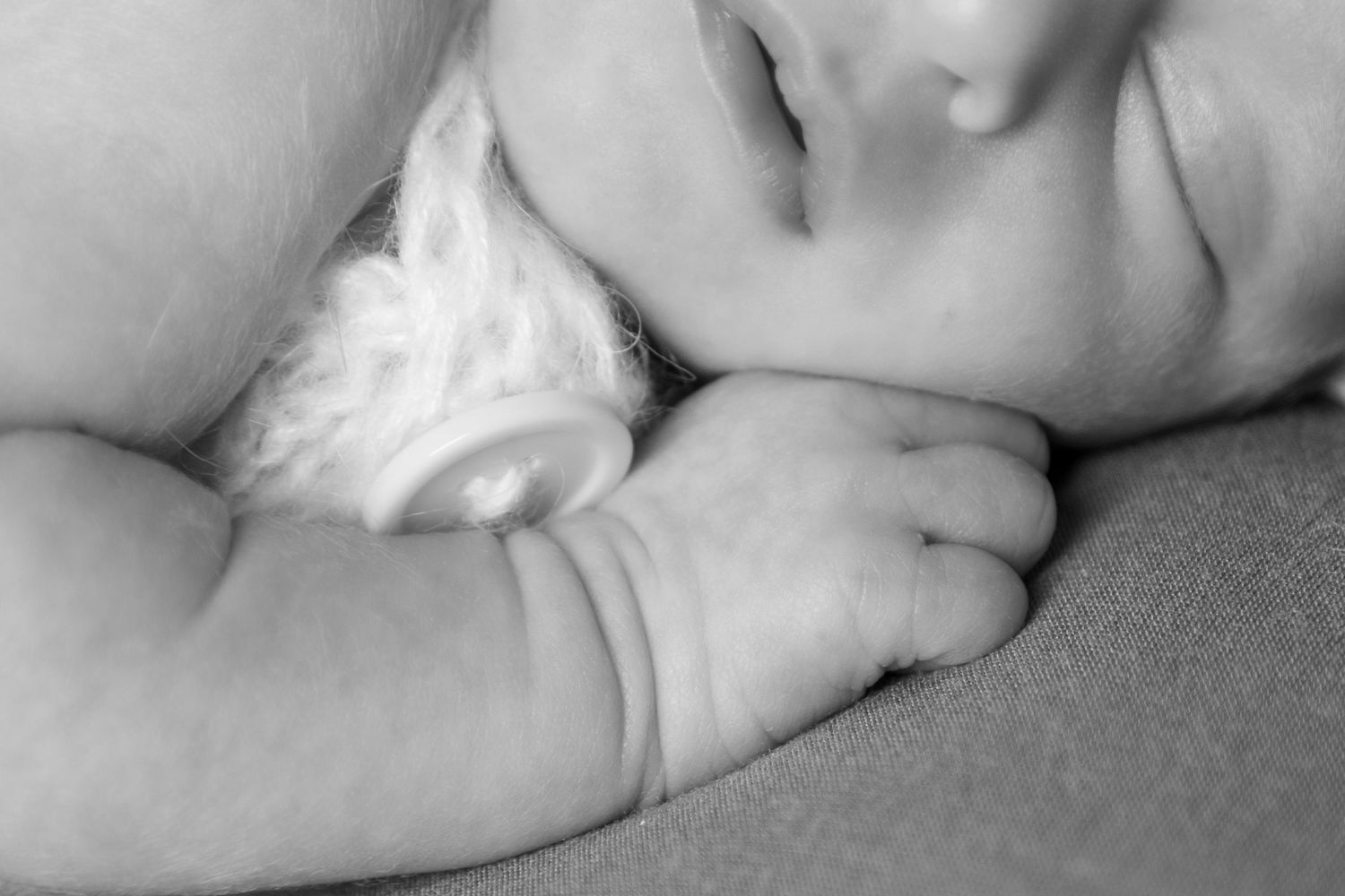 Black and white close-up of a sleeping baby with a peaceful expression. The baby is holding a knitted blanket.