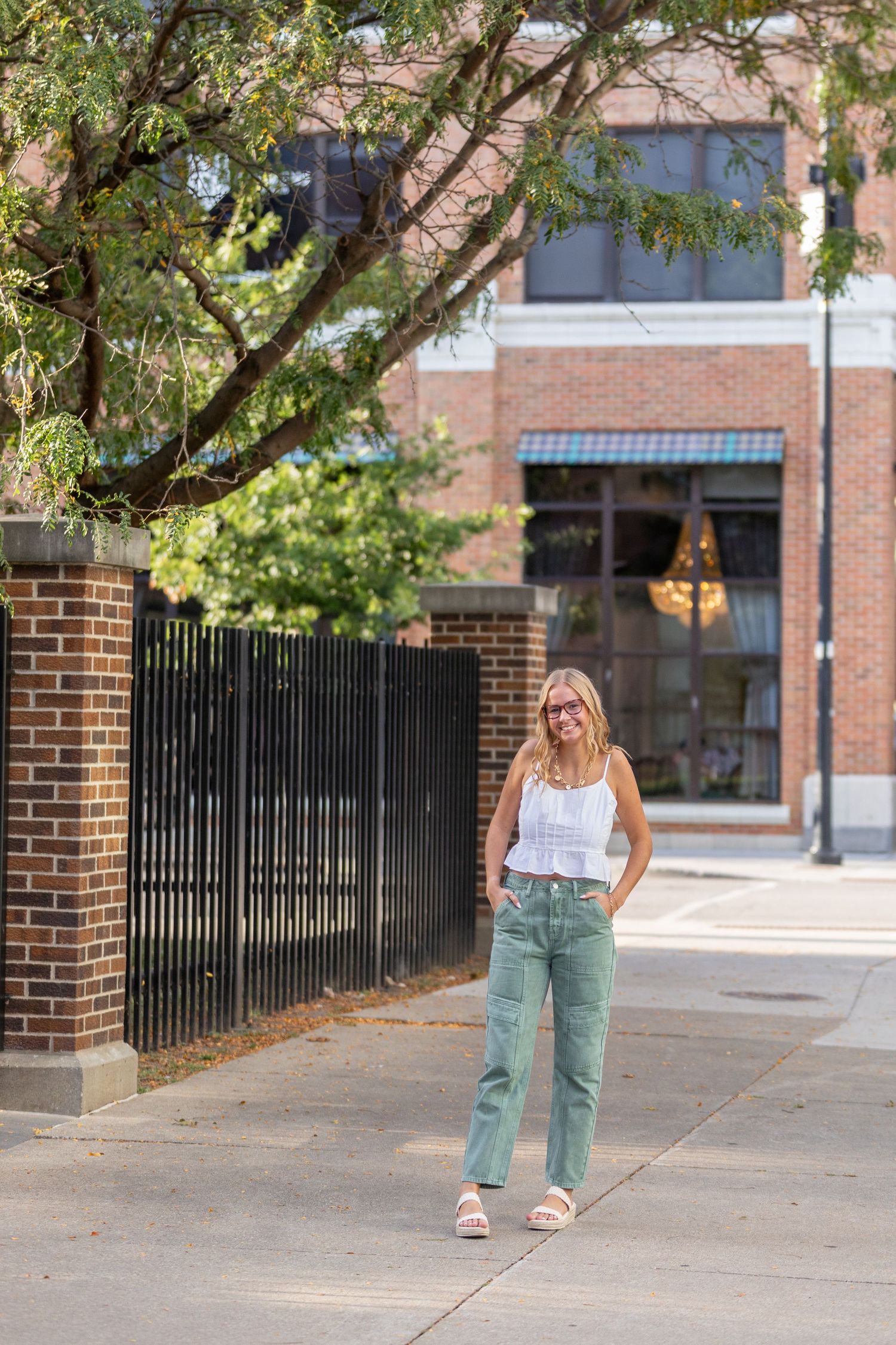 A high school senior walks along the sidewalk by a wrought iron fence in downtown Des Moines, Iowa