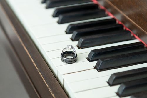 Two wedding rings rest on white piano keys, symbolizing love and harmony. The scene is elegant and serene.