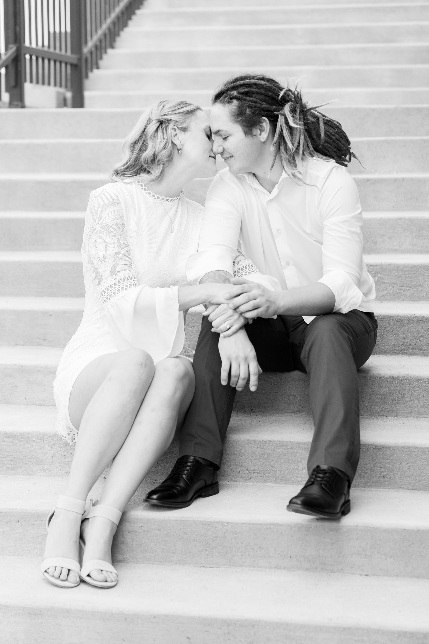 A couple sits closely on stairs, smiling at each other in an affectionate manner in Des Moines, Iowa.