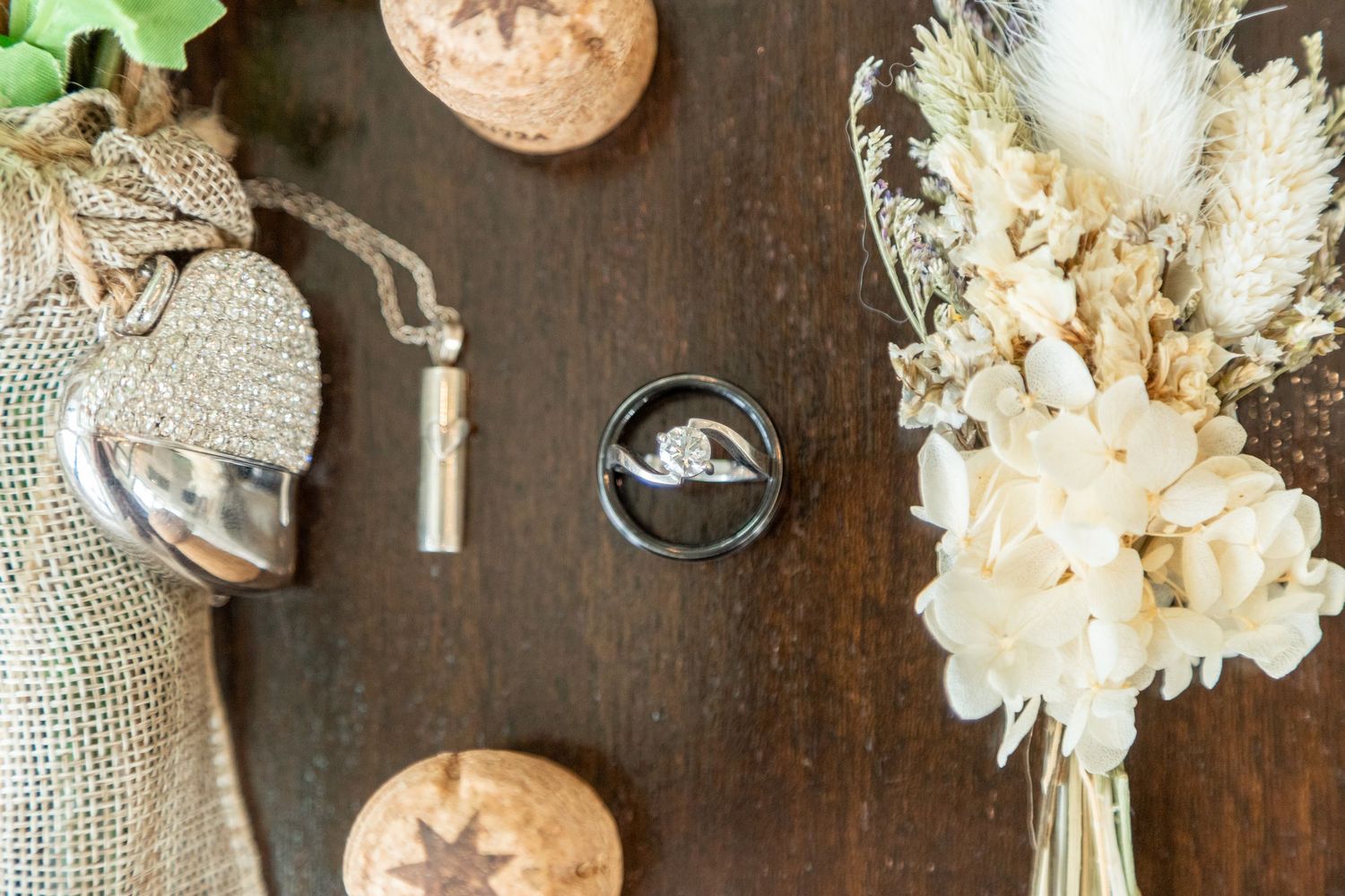 Vintage items and a wedding ring on a wooden table. On the left, a burlap bag with a locket. On the right, dried flowers.