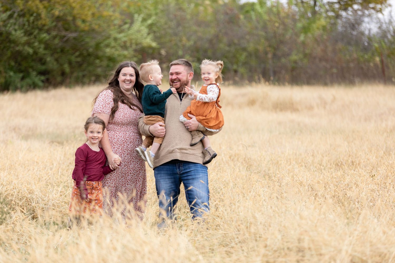 A family of five, with two children held by parents, standing in a golden field in Adel, Iowa.