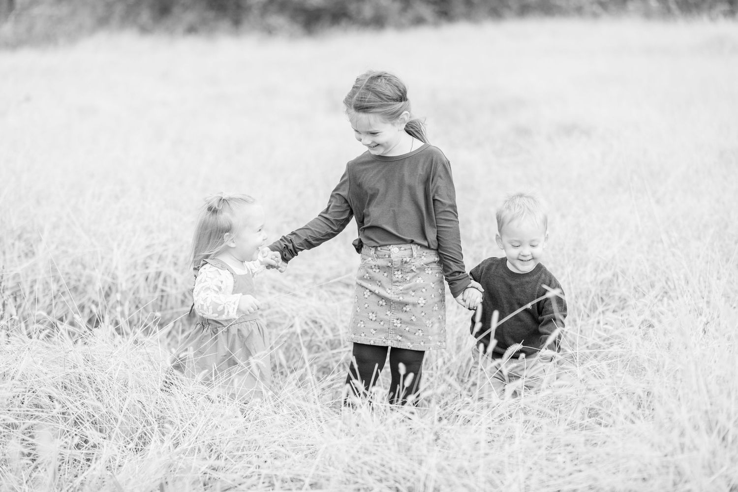 Three children stand hand in hand in a prairie grass field in Adel, Iowa.
