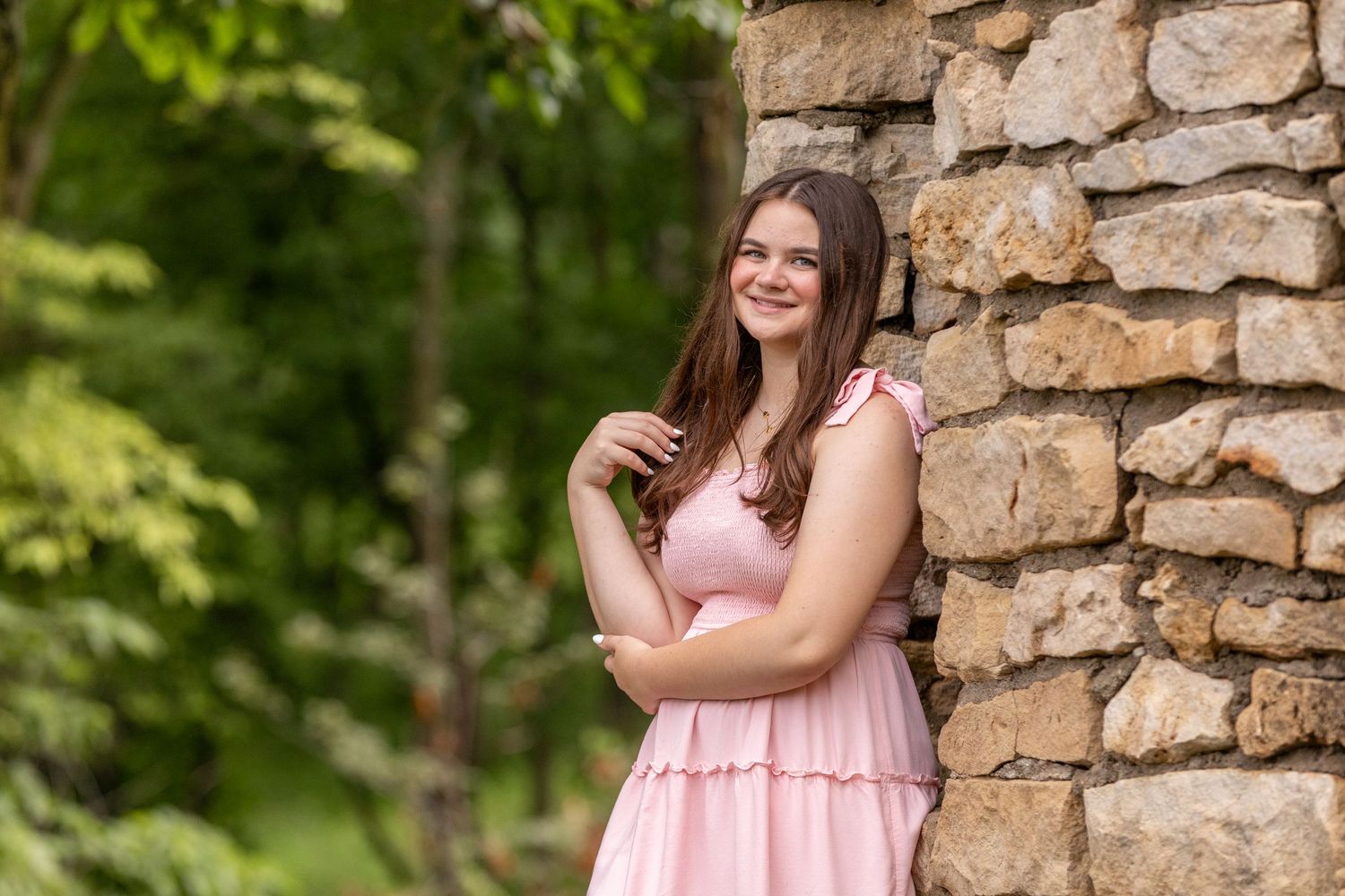 A high school senior in a pink dress leans against the Historic Clark Tower in Winterset, Iowa.