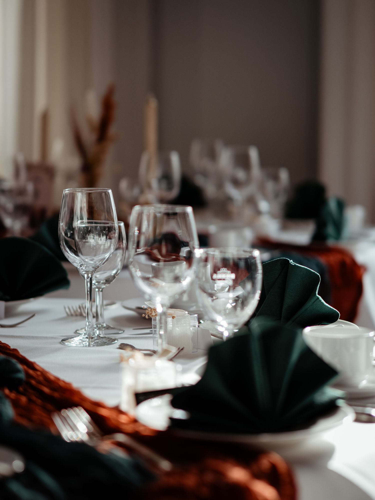 Elegant wedding reception table set with crystal wine glasses, dark green napkins, and white linen tablecloth.