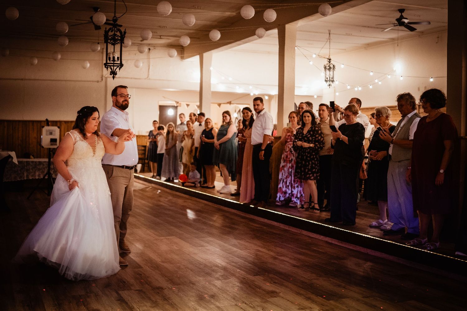 Bride and groom preparing for bouquet toss surrounded by guests in a warmly lit reception hall.