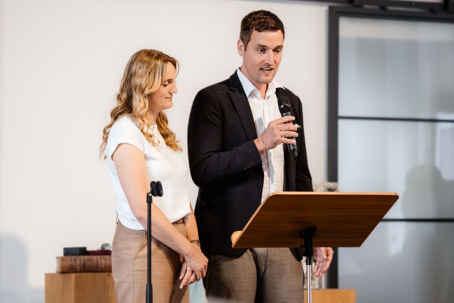 Man and woman presenting at a podium with a microphone in a modern conference room.