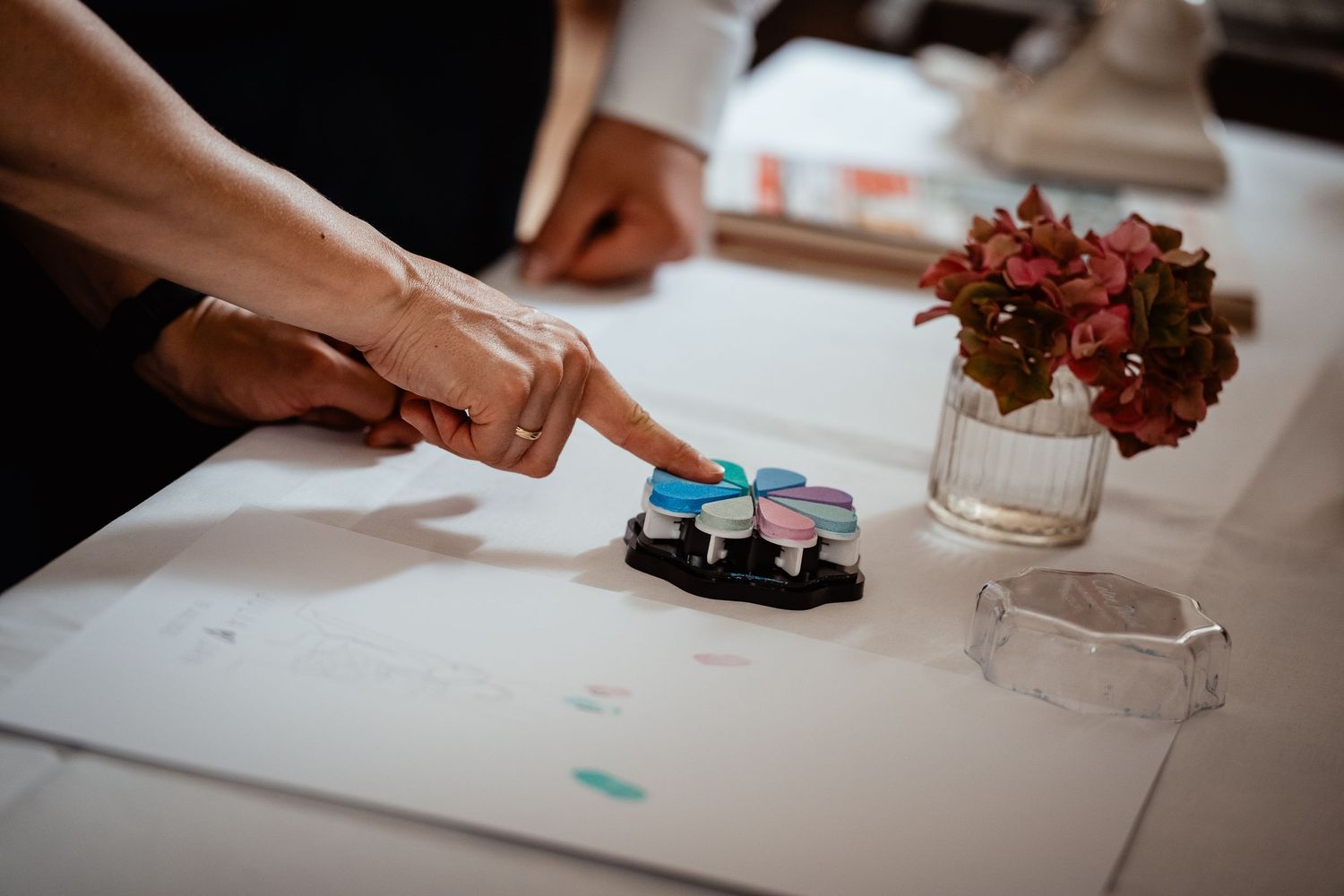 Person pressing colorful button device on white table with floral arrangement at wedding reception.