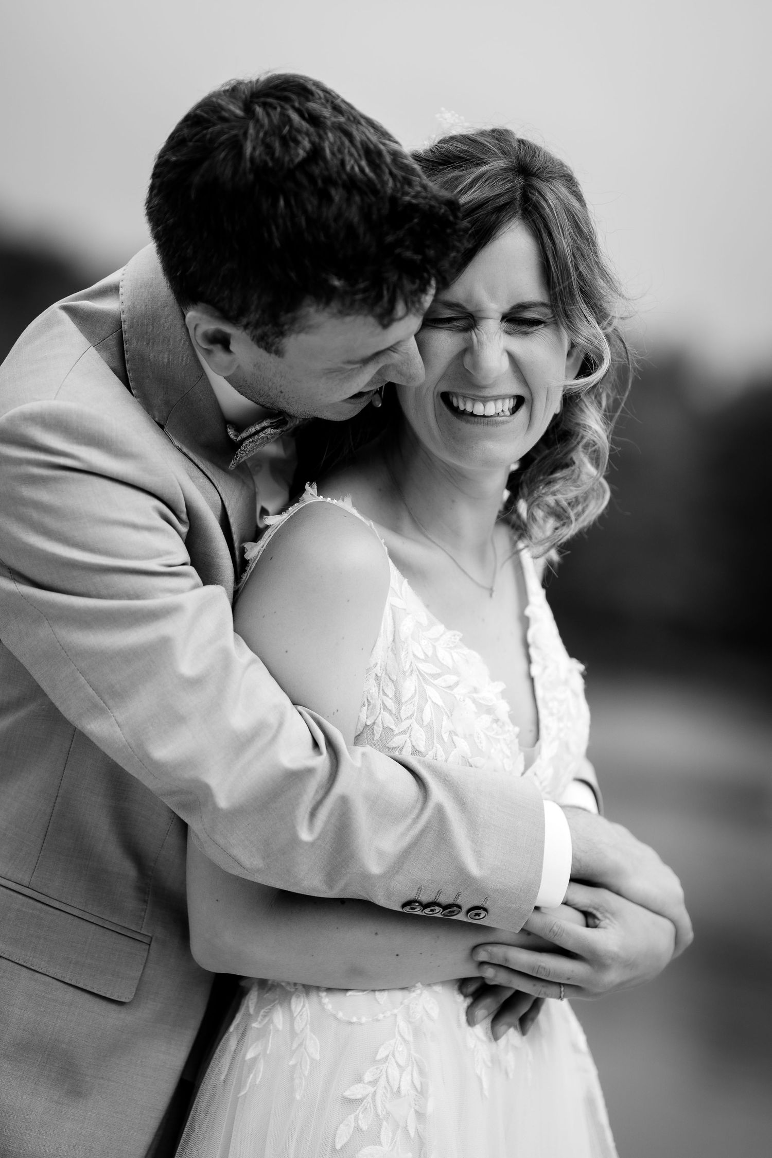 Groom tenderly embraces laughing bride in black and white wedding portrait.