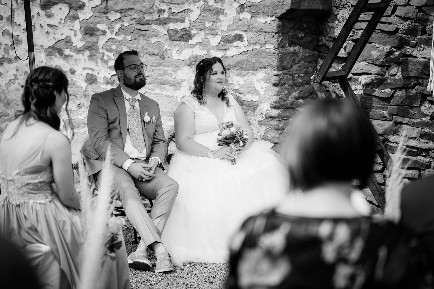 Black and white photo of bride and groom seated together during an intimate wedding ceremony in a stone venue.
