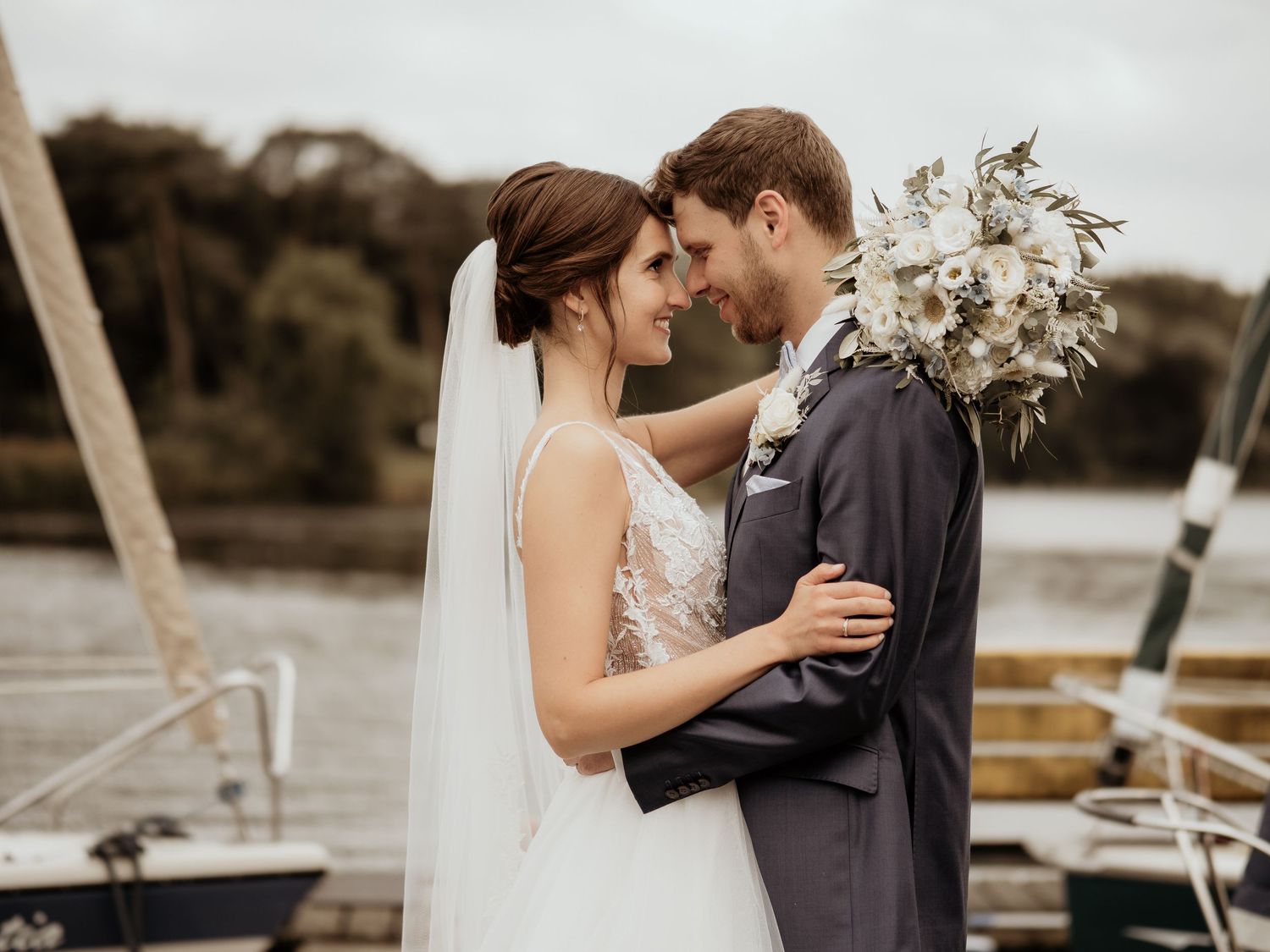 A romantic wedding moment captured on a dock with boats in the background during golden hour.