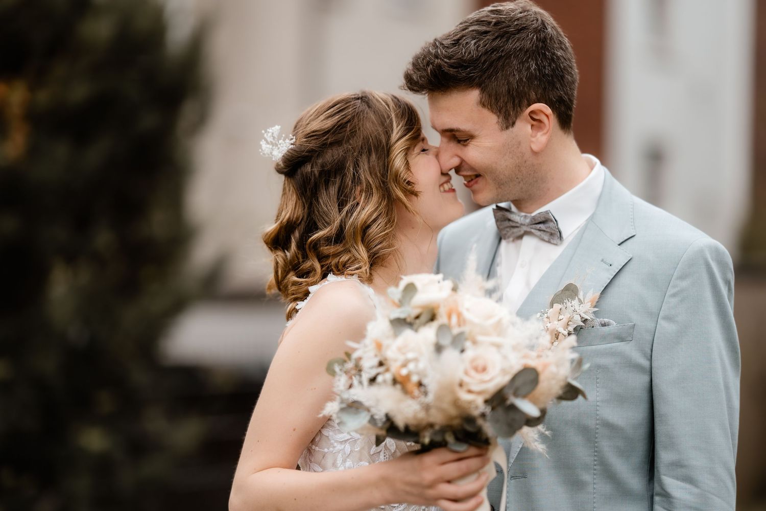 Bride and groom sharing a romantic moment outdoors, groom in light blue suit, bride holding bouquet.