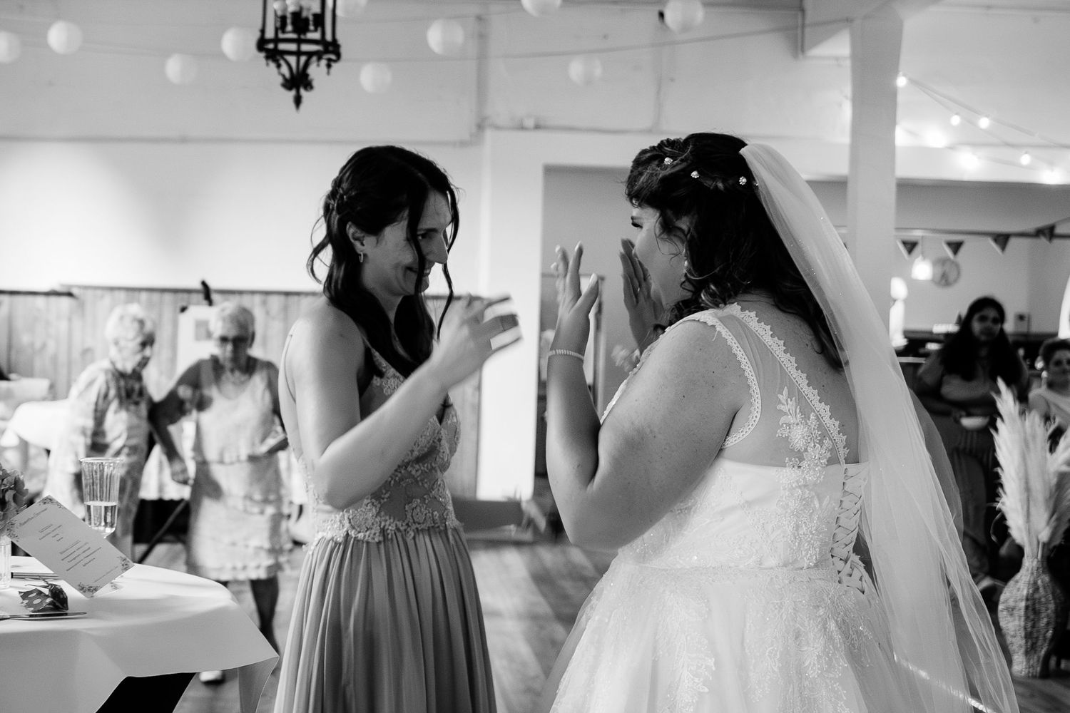 Bridesmaid and emotional bride sharing tender moment in black and white wedding reception photo.