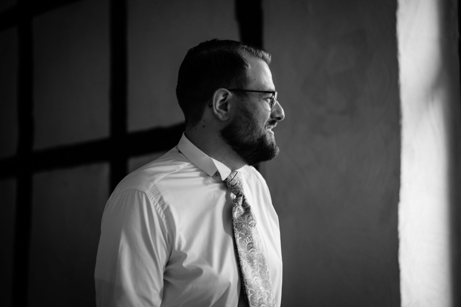 Black and white portrait of a bearded man in a dress shirt and tie gazing thoughtfully to the side.