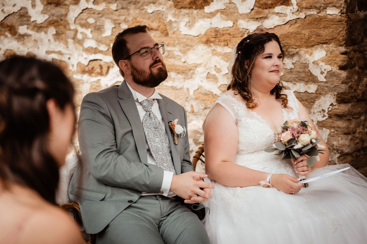 Bride and groom seated together during wedding ceremony in rustic stone venue.