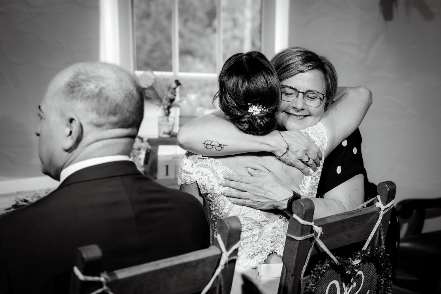 Black and white photo of a bride embracing a smiling female guest during the wedding ceremony.