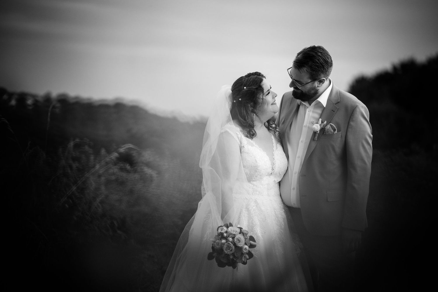 Romantic black and white portrait of bride and groom gazing at each other in outdoor field.