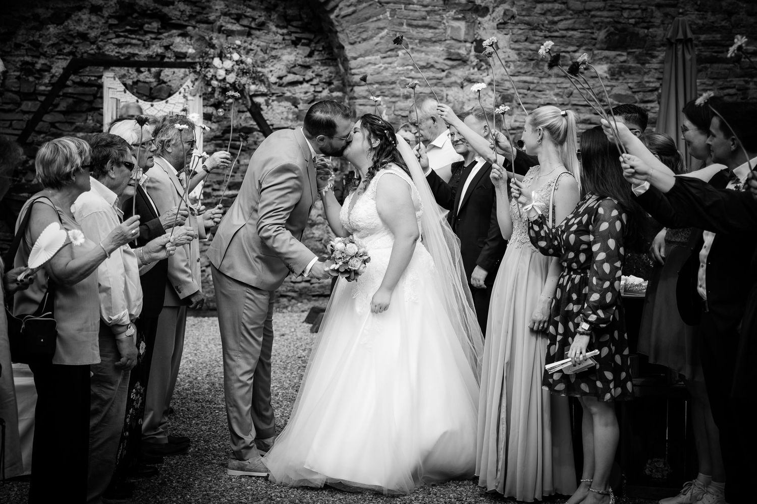 Black and white wedding photo of bride and groom walking through a confetti line of cheering guests.