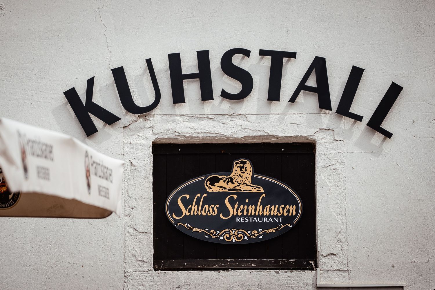 Kuhstall restaurant sign with Schloss Steinhausen logo on a white wall.